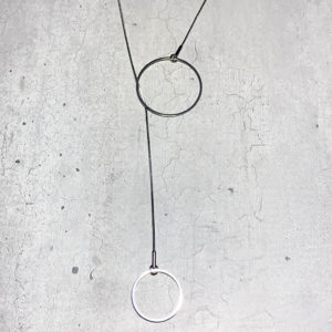 steel lariat pendant with two circles of different sizes on a grey concrete backround