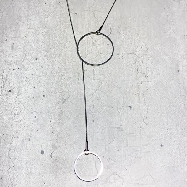 steel lariat pendant with two circles of different sizes on a grey concrete backround
