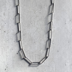 A long paperclip style steel chain on a grey concrete background