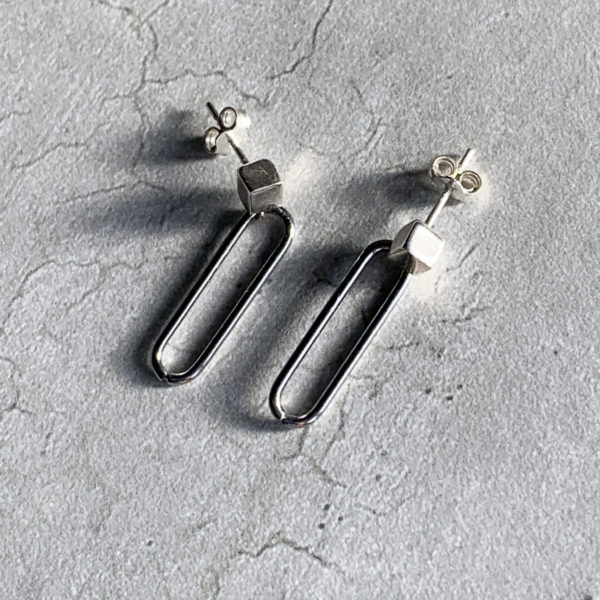 steel paperclip earrings on silver cubes, concrete background