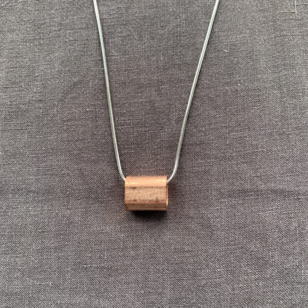 chunky steel pendant featuring a copper tube on a linen background