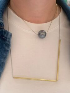 A woman wearing Factory Floor Jewels brass L pendant with another pendant of her own