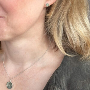 a photo of a blonde woman wearing a small silver stud earring and a matching pendant featuring small flakes of repurposed aluminium.