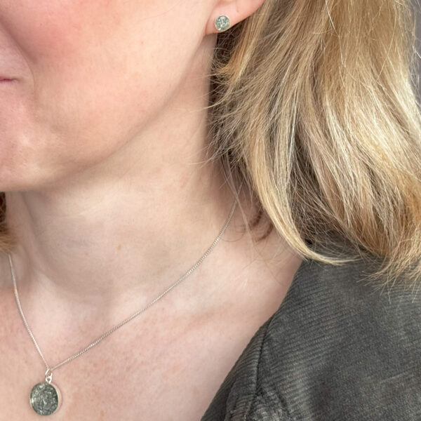 a photo of a blonde woman wearing a small silver stud earring and a matching pendant featuring small flakes of repurposed aluminium.