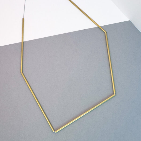 A statement brass necklace featuring 5 delicate pipes strung on steel chain, creating an asymmetric statement piece