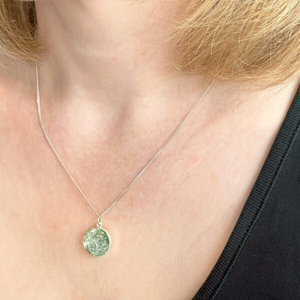 a blonde woman wearing a sparkly silver pendant - the photos only shows her neck and the pendant