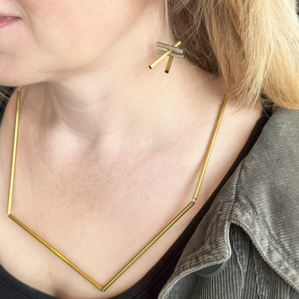 a blond woman wearing a striking asymmetric brass necklace and matching dangle earrings