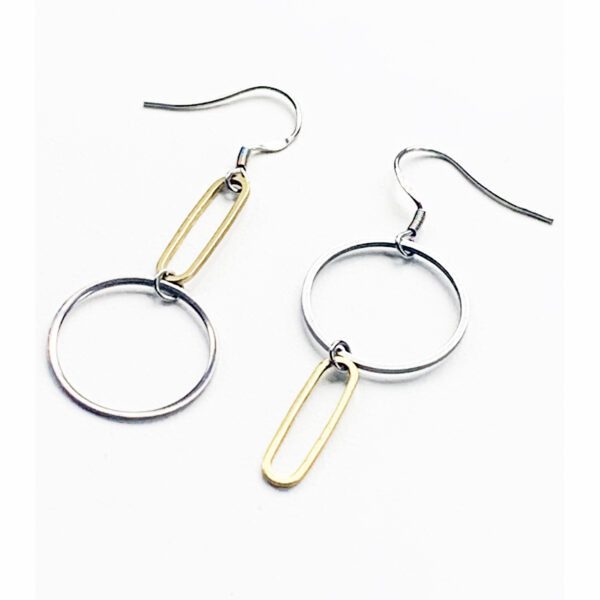 A pair of Factory Floor Jewels mismatched earrings in steel and brass on a white background