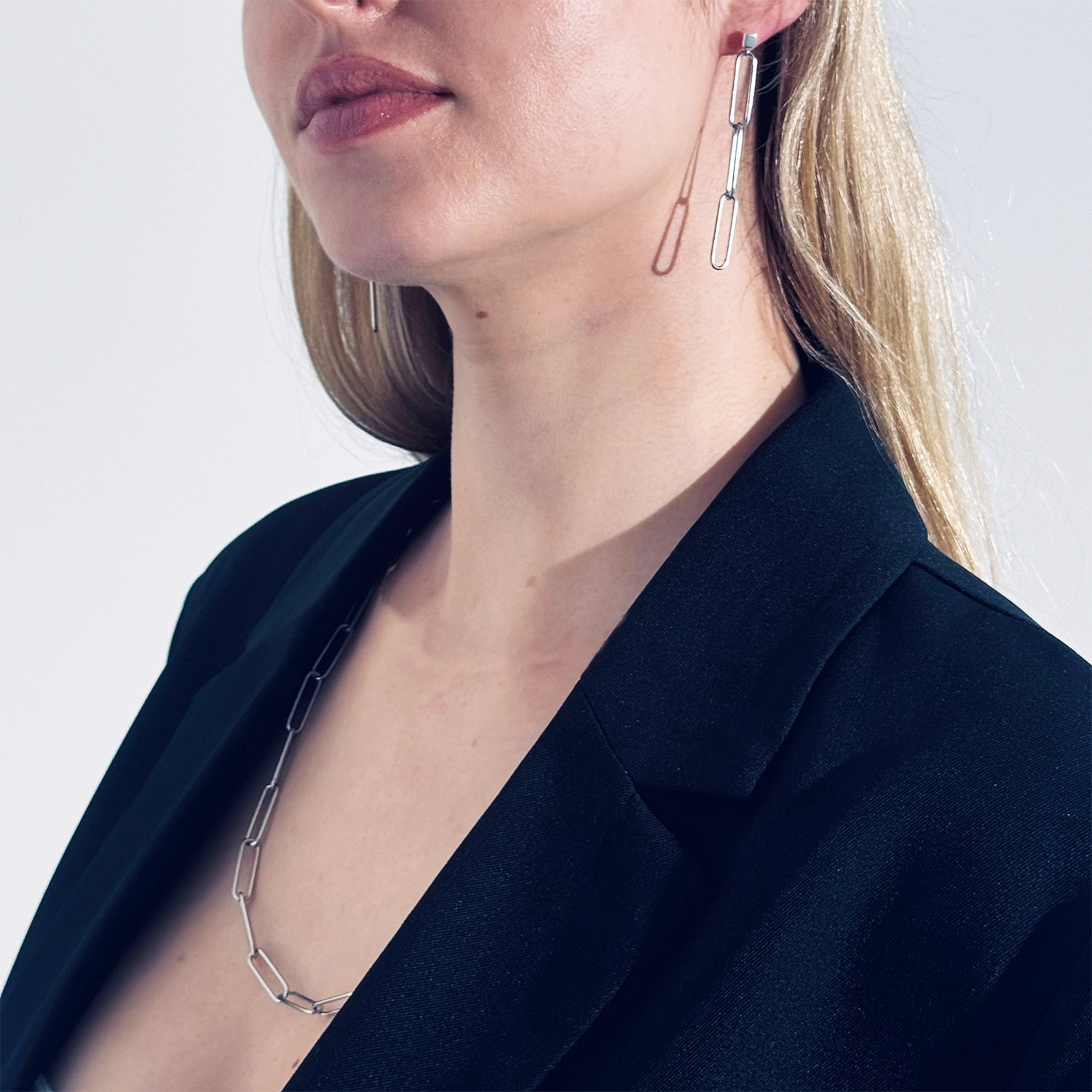 blonde woman in black jacket wearing steel paperclips chain and earrings